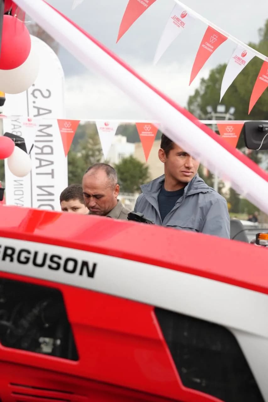 Kırmızı Massey Ferguson traktörün logosu ve arkasında bekleyen ziyaretçiler